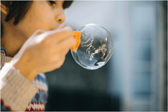 Young girl holding a bubble wand and blowing a bubble.